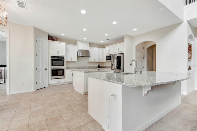 kitchen featuring arched walkways, under cabinet range hood, a spacious island, a sink, and appliances with stainless steel finishes