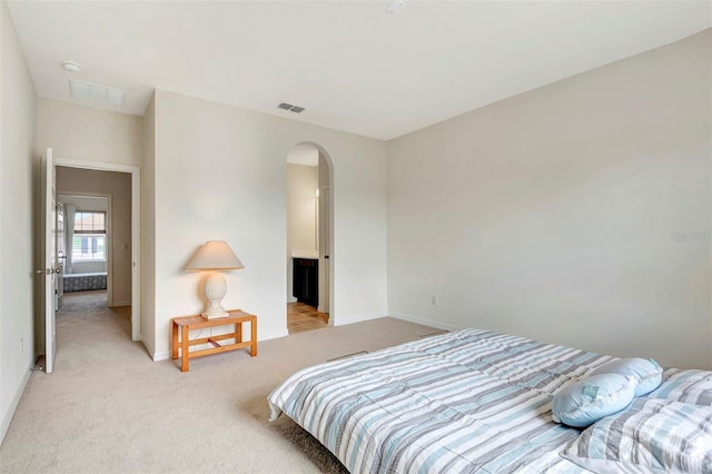 bedroom featuring light colored carpet, arched walkways, visible vents, and baseboards