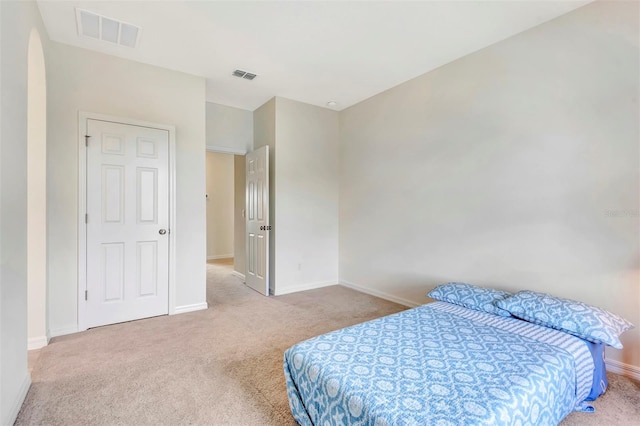 carpeted bedroom with arched walkways, visible vents, and baseboards