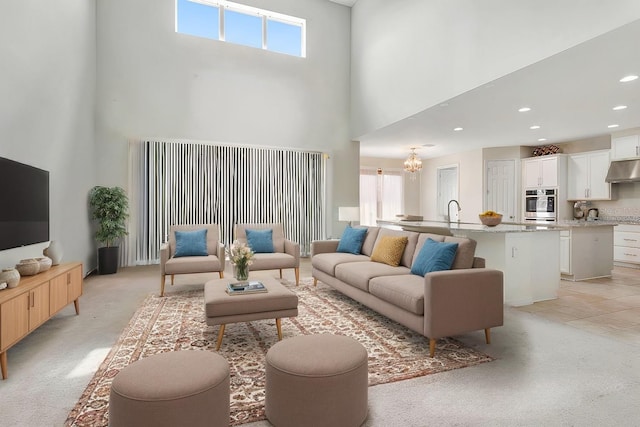 living area featuring a healthy amount of sunlight, a towering ceiling, a notable chandelier, and light colored carpet