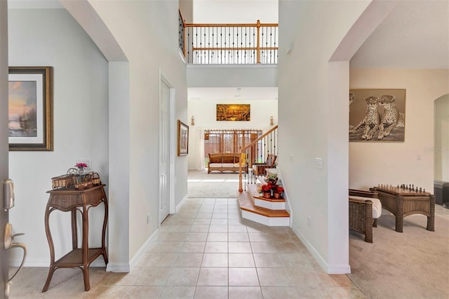 entrance foyer with arched walkways, light tile patterned floors, light carpet, a high ceiling, and stairs