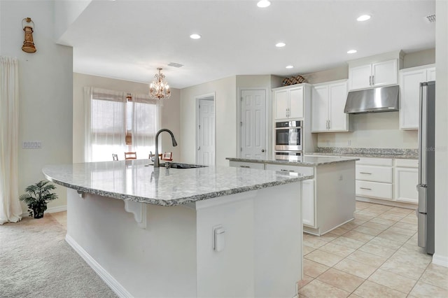 kitchen with under cabinet range hood, a sink, white cabinets, appliances with stainless steel finishes, and a center island with sink