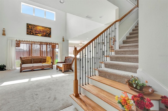 stairway with carpet floors, a healthy amount of sunlight, visible vents, and a high ceiling