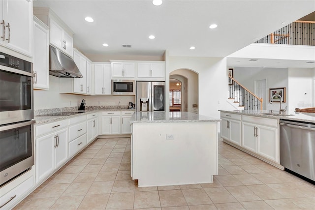 kitchen with light tile patterned floors, a center island, stainless steel appliances, under cabinet range hood, and a sink