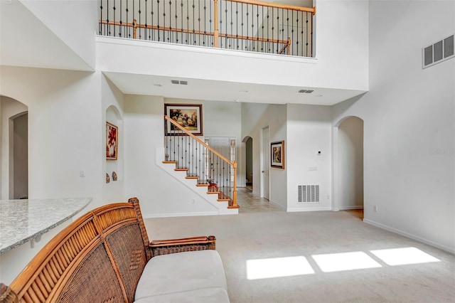 carpeted entryway featuring stairs, a high ceiling, visible vents, and arched walkways