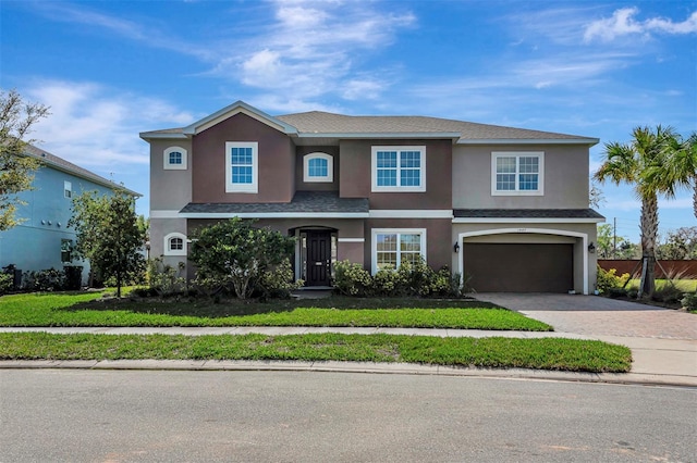 traditional home with a garage, fence, decorative driveway, stucco siding, and a front yard