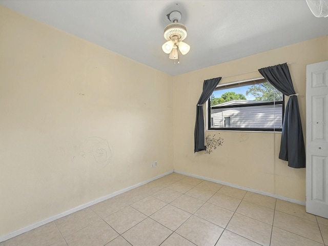 tiled empty room featuring a ceiling fan and baseboards