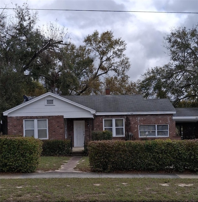 view of front of property with a shingled roof, brick siding, and a chimney