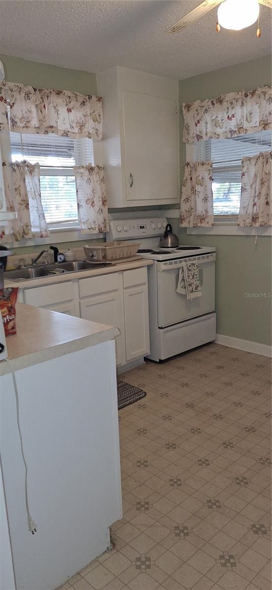 kitchen with light countertops, white range with electric stovetop, a healthy amount of sunlight, and white cabinets