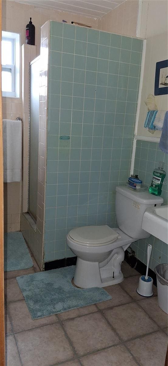 bathroom with toilet, a stall shower, and tile walls