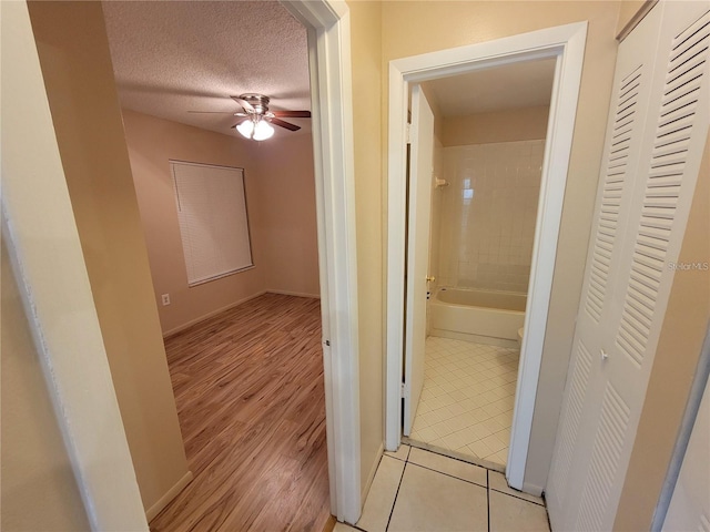 hall with a textured ceiling, baseboards, and light tile patterned floors