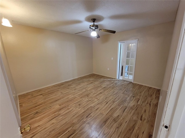 empty room featuring a textured ceiling, ceiling fan, light wood-style flooring, and baseboards