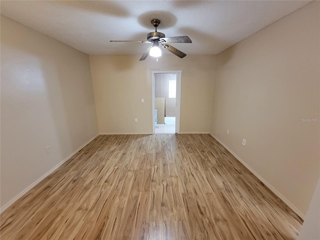 spare room featuring light wood finished floors, a textured ceiling, baseboards, and a ceiling fan