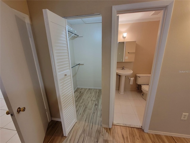 half bath with a walk in closet, toilet, a sink, wood finished floors, and baseboards