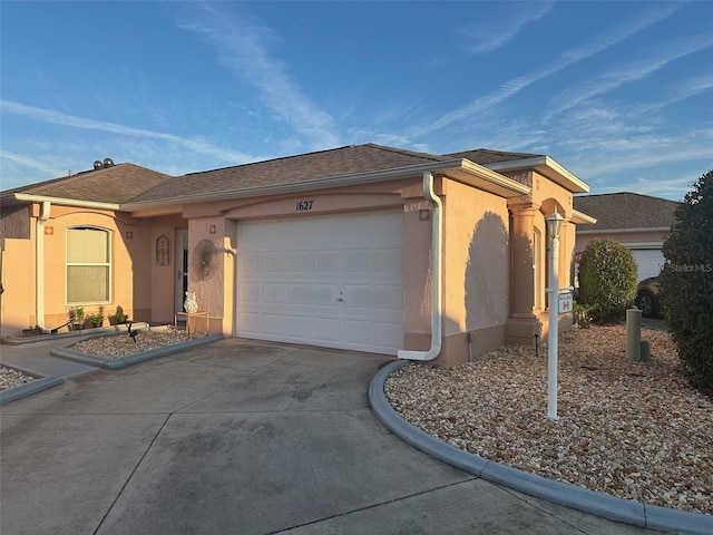 single story home with an attached garage, a shingled roof, concrete driveway, and stucco siding