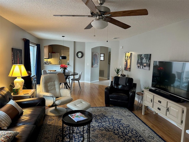 living area featuring arched walkways, visible vents, a textured ceiling, and light wood finished floors