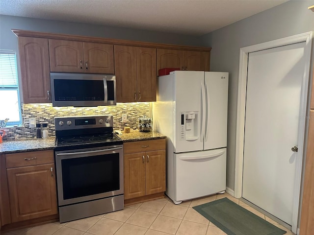 kitchen with stone countertops, stainless steel appliances, backsplash, and light tile patterned flooring