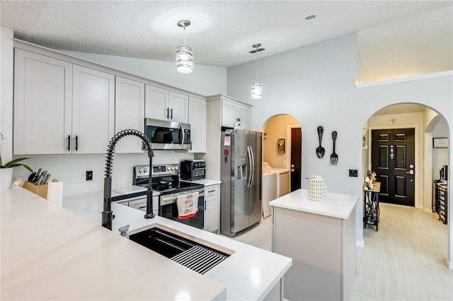 kitchen with arched walkways, light countertops, appliances with stainless steel finishes, a kitchen island, and washer and dryer