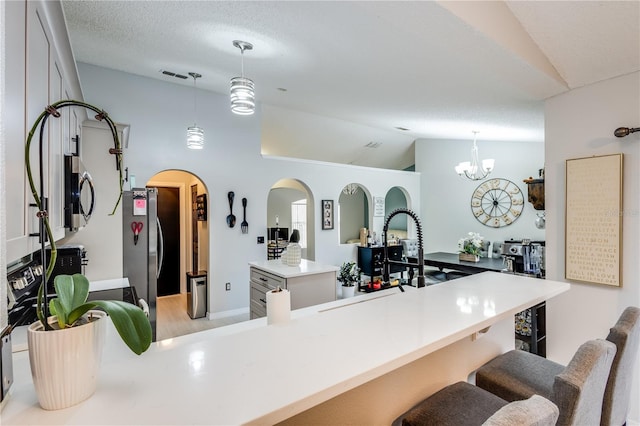 kitchen featuring lofted ceiling, a textured ceiling, stainless steel appliances, visible vents, and a kitchen bar