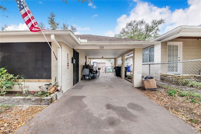 view of home's exterior with concrete block siding, concrete driveway, a sunroom, fence, and a carport