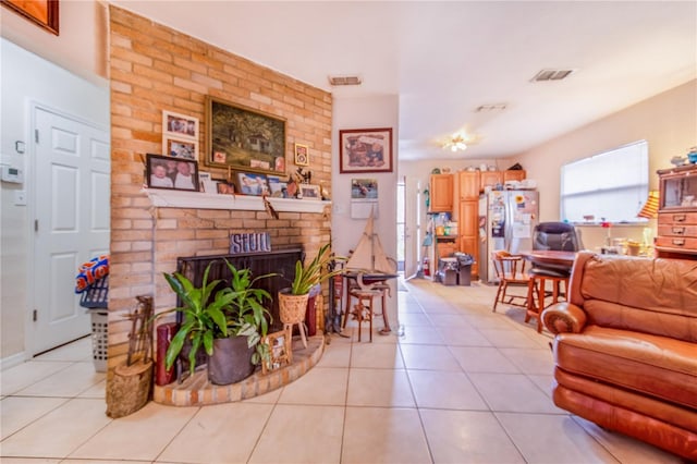 living room with a brick fireplace, visible vents, and light tile patterned flooring