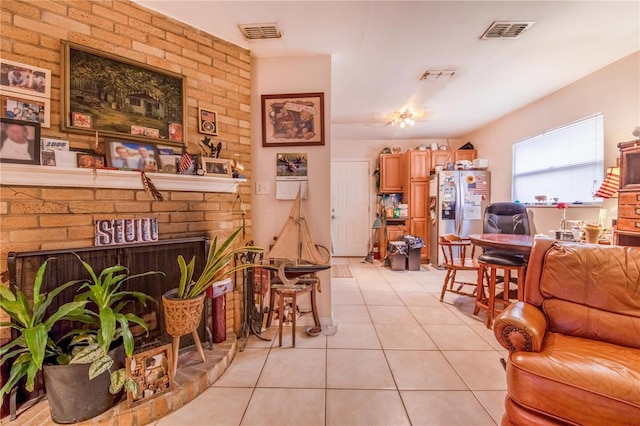 living area featuring light tile patterned floors, a brick fireplace, and visible vents