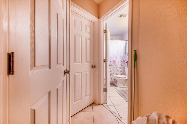 hallway featuring light tile patterned floors, a textured wall, and visible vents