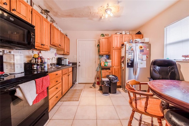 kitchen featuring dark countertops, black appliances, light tile patterned floors, and a sink