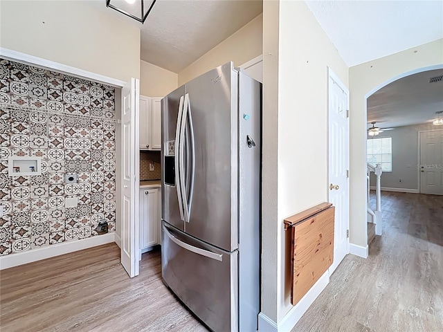 kitchen with light wood-type flooring, stainless steel refrigerator with ice dispenser, white cabinetry, arched walkways, and baseboards