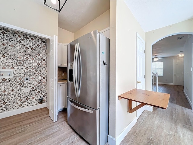 kitchen featuring baseboards, light wood finished floors, lofted ceiling, arched walkways, and stainless steel fridge