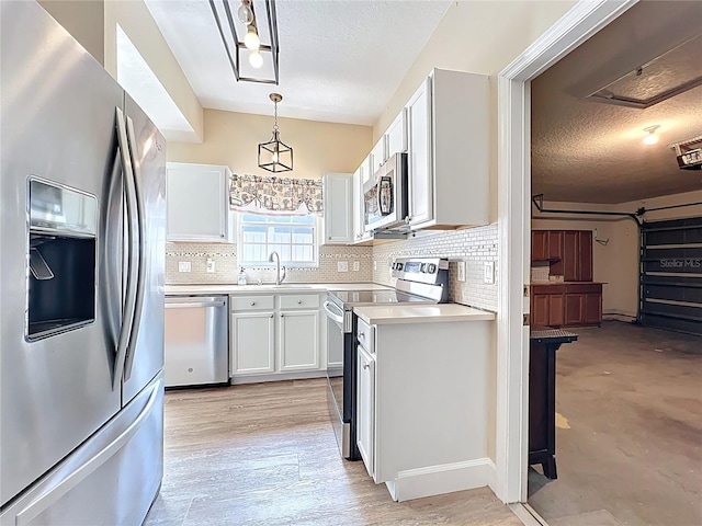 kitchen with stainless steel appliances, light countertops, white cabinets, a textured ceiling, and decorative light fixtures