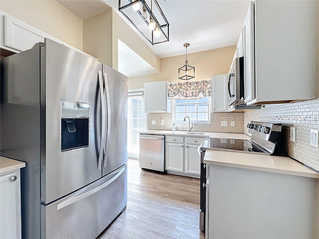 kitchen with light wood-type flooring, a sink, tasteful backsplash, appliances with stainless steel finishes, and hanging light fixtures