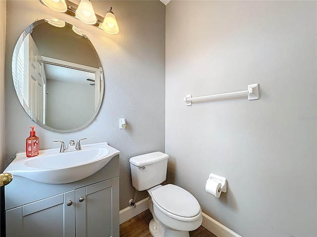 half bathroom with baseboards, toilet, wood finished floors, and vanity