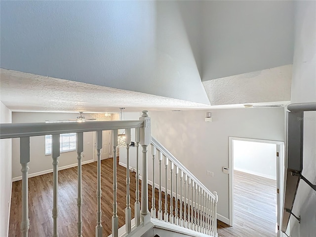 staircase featuring baseboards, a textured ceiling, and wood finished floors