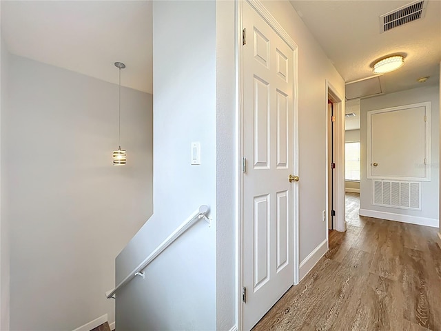 hallway featuring wood finished floors, an upstairs landing, visible vents, and baseboards