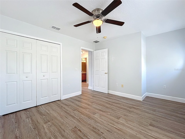 unfurnished bedroom with wood finished floors, visible vents, a closet, and baseboards