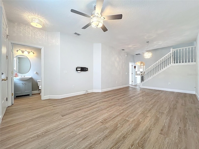 unfurnished living room featuring baseboards, visible vents, light wood finished floors, a sink, and stairs