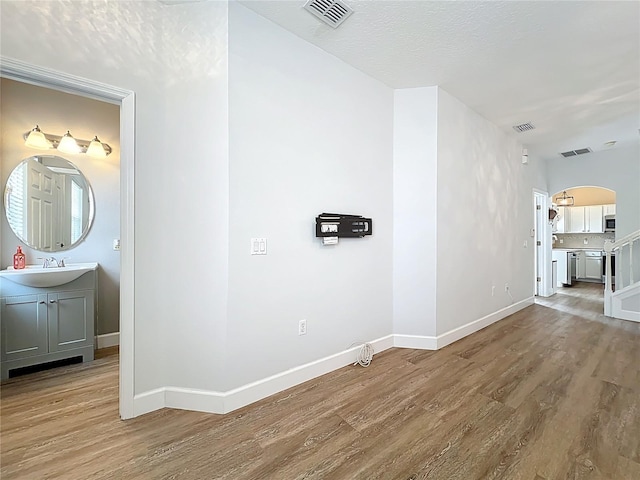 corridor featuring arched walkways, visible vents, a sink, and wood finished floors