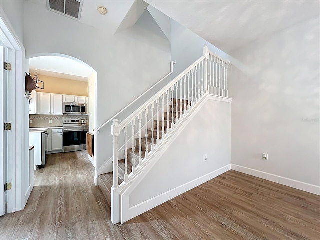 stairway featuring visible vents, baseboards, arched walkways, and wood finished floors