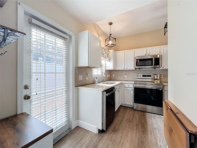 kitchen with wood finished floors, a sink, decorative backsplash, appliances with stainless steel finishes, and white cabinetry