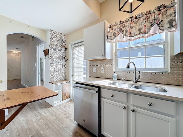 kitchen featuring a sink, tasteful backsplash, wood finished floors, arched walkways, and dishwasher