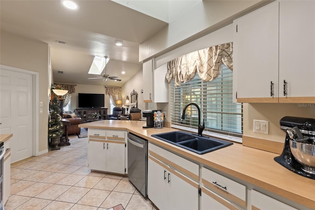 kitchen featuring a skylight, a sink, white cabinets, light countertops, and dishwasher