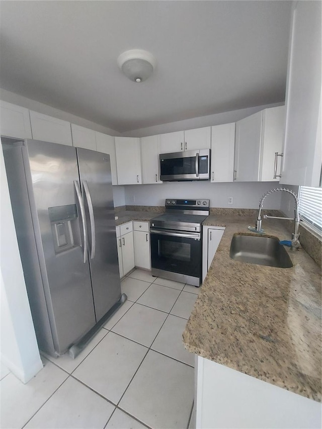 kitchen with light tile patterned floors, appliances with stainless steel finishes, a sink, and white cabinetry