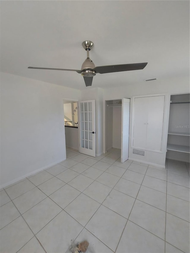 unfurnished bedroom with light tile patterned flooring, ceiling fan, baseboards, and two closets