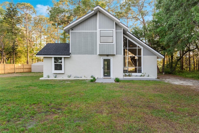 rear view of property with a lawn, roof with shingles, and fence