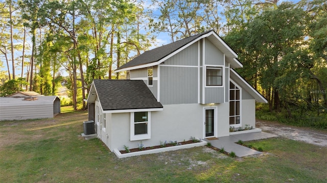 back of property featuring a yard, roof with shingles, and central AC