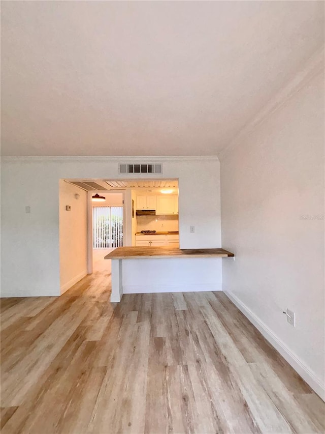 unfurnished living room featuring ornamental molding, light wood-type flooring, visible vents, and baseboards