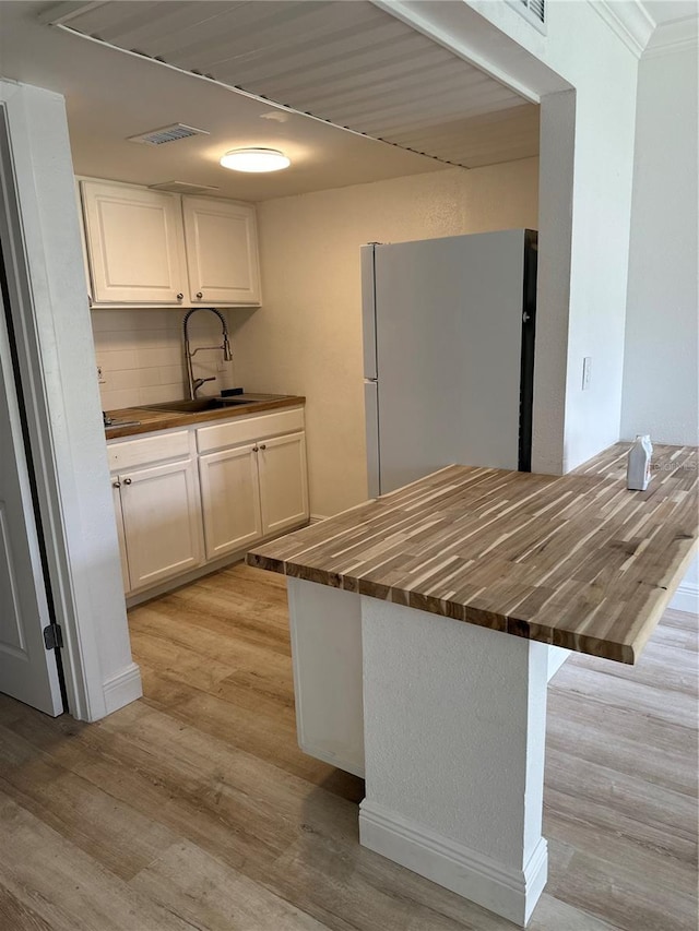 kitchen with freestanding refrigerator, white cabinets, a sink, butcher block countertops, and light wood-type flooring