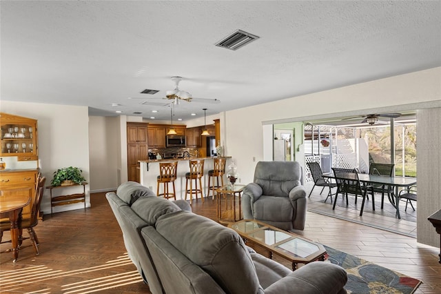 living area featuring dark wood-style floors, visible vents, ceiling fan, and a textured ceiling