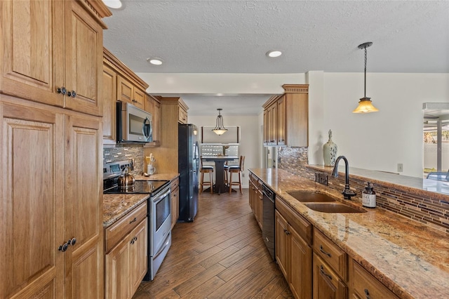 kitchen with light stone counters, a sink, appliances with stainless steel finishes, tasteful backsplash, and dark wood finished floors